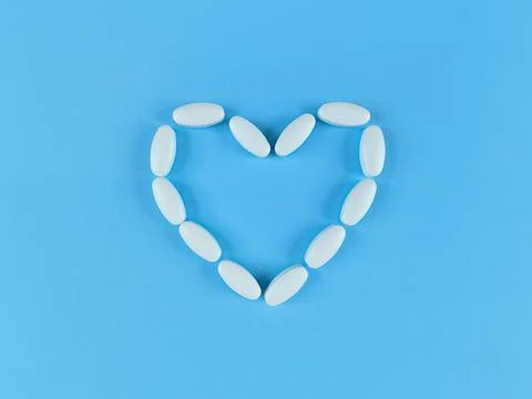 Heart shape made from white tablets on blue backdrop. Stock Photos
