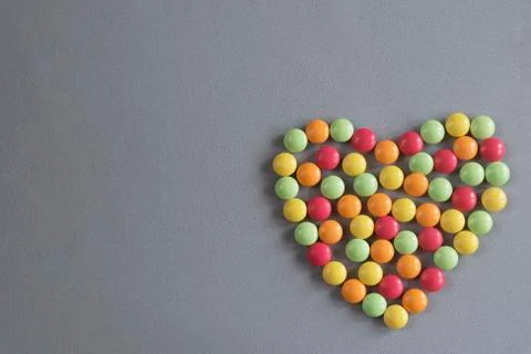 Heart shape from multi-colored tablets of dragees on a gray woven background Stock Photos