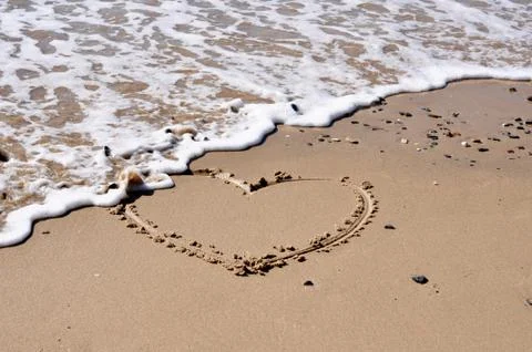 A heart shape in the sand being eroded by the sea Stock Photos