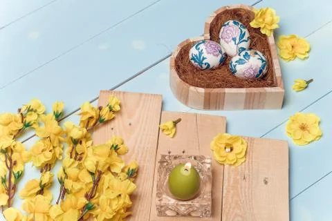 Heart shaped box with decorated Easter eggs, yellow flowers, burning candle Stock Photos