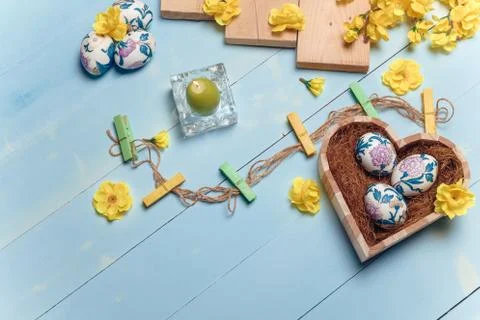 Heart shaped box with decorated Easter eggs, yellow flowers, burning candle Stock Photos
