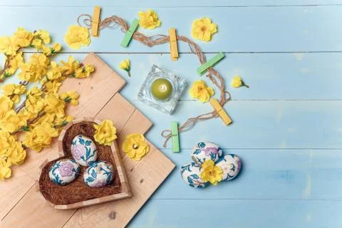 Heart shaped box with decorated Easter eggs, yellow flowers, burning candle Stock Photos
