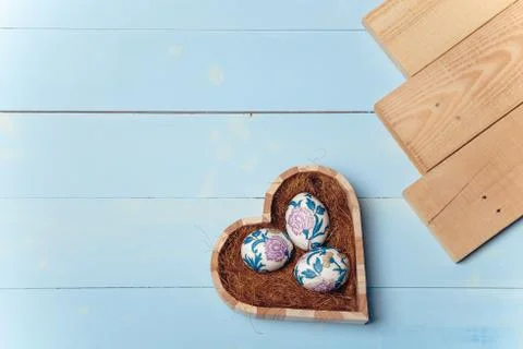 Heart shaped box with decorated Easter eggs and brown boards on wooden blue Stock Photos