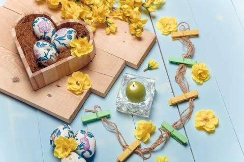 Heart shaped box with decorated Easter eggs, yellow flowers, burning candle Stock Photos