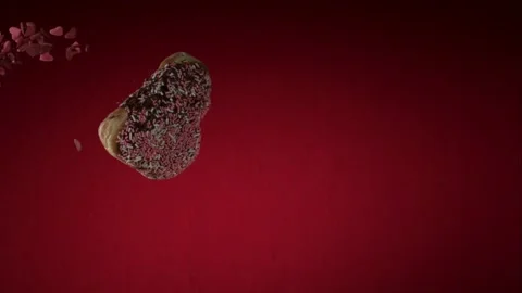 Heart shaped chocolate donuts falling against a red background Stock Footage 327631792