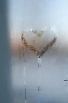 A heart-shaped clear patch melted into frosty glass Foto stock