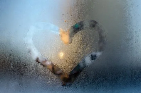 A heart-shaped clear patch melted into frosty glass Foto stock