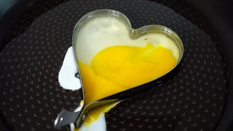 Heart shaped fried yellow egg on black hot pan. Appetizing breakfast. 스톡 동영상 89034563
