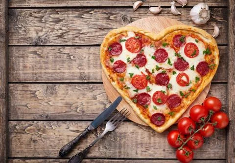 Heart shaped pizza with pepperoni, tomatoes and mozzarella on vintage wooden Stock Photos