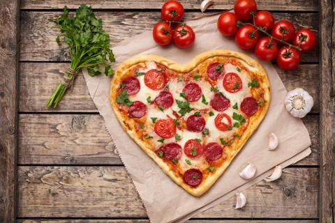 Heart shaped pizza with pepperoni, tomatoes, mozzarella, garlic and parsley Stock Photos
