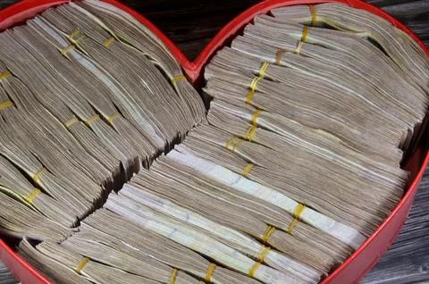 A heart shaped red box full of stacks and piles of money bills banknotes fi.. Stock Photos