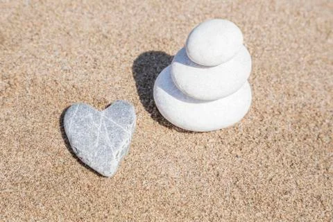 Heart shaped stone and stack of pebbles on balance on sand Stock Photos