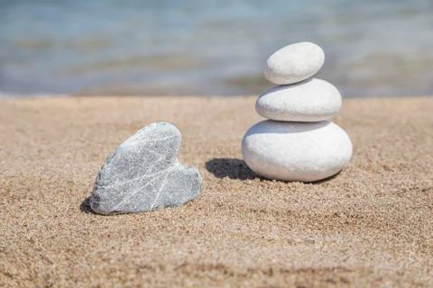 Heart shaped stone and stack of pebbles on balance on sandy beach Stock Photos