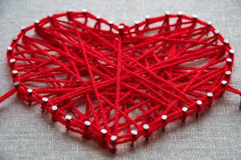 Heart shaped string art crafted from red yarn wrapped over metal nails Foto stock