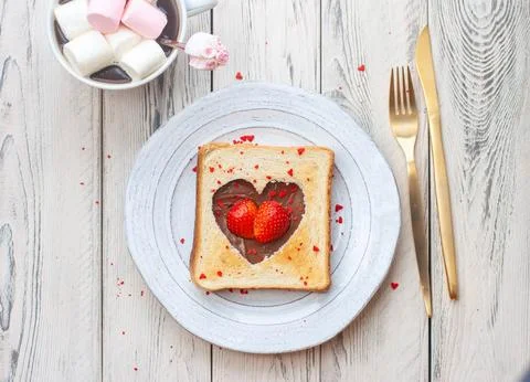 Heart shaped toasted bread with nutella and fresh strawberry on wooden table Stock Photos