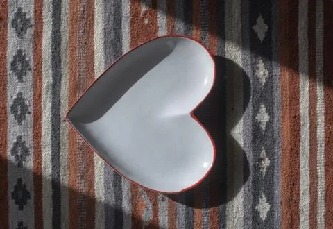 Heart shaped white plate with red edge on rustic rug Foto stock