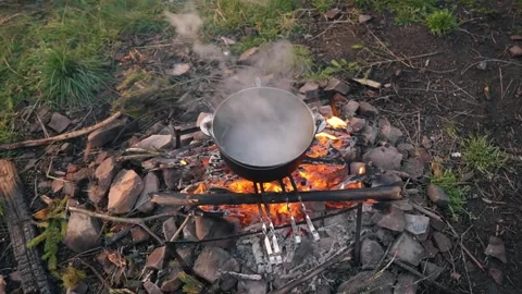 A hearth is burning, on which a cauldron of food is being cooked. Food on fire Stock Footage 272512612