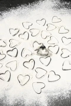 Hearts from a cookie baking dish are drawn and laid out on the scattered flour Stock Photos