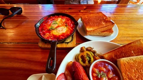 Hearty breakfast spread with toast, eggs, bacon, sausages, baked beans, and Stock Footage 333779020