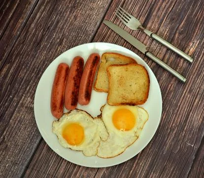 A hearty breakfast: two fried eggs, sausages, and toasted bread on a plate .. Stock Photos