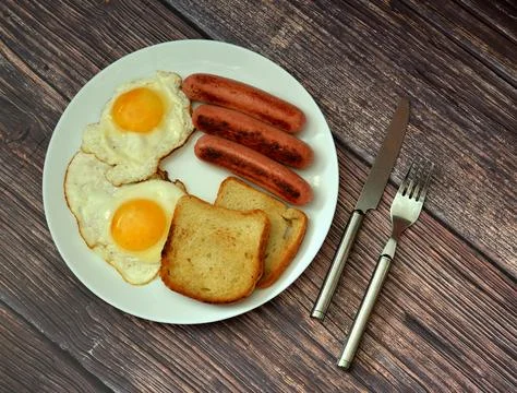 A hearty breakfast: two fried eggs with sausages and toasted bread in a rou.. Stock Photos