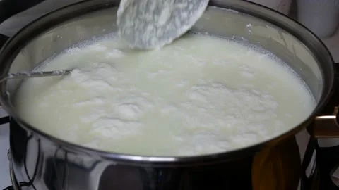 Heated milk coagulates and light green liquid occurs over the milk Stock Footage 145373657