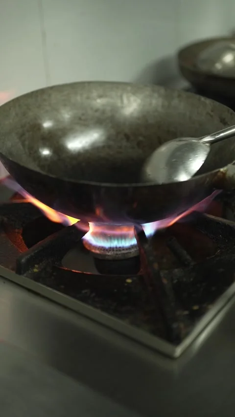 Heating an Empty Iron Wok Over a High Gas Flame With a Cooking Ladle Stock Footage 346678327