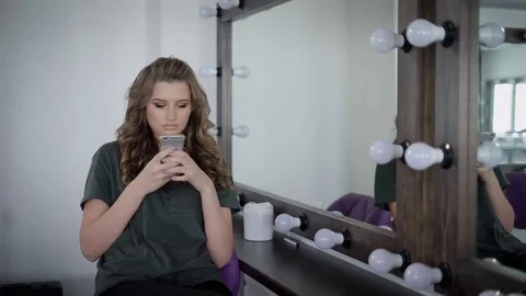 Heavily made girl with full lips sitting near mirror with lamps in the dressing Stock Footage