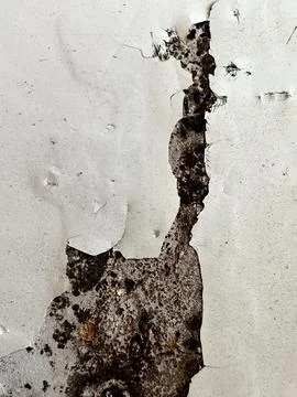 Heavily weathered white wall with peeling paint exposing dark rusty metal Stock Photos