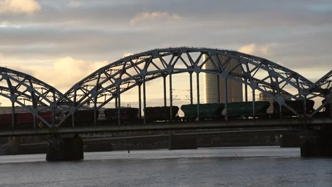 Heavy cargo train moving across metal railway bridge structure in Riga Stock Footage 320803941