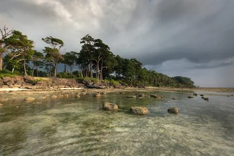 Heavy clouds and low tide at the scenic rocky coast of a tropical island Stock Photos