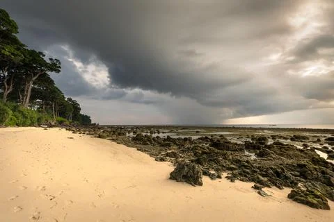 Heavy clouds and low tide at the scenic rocky coast of a tropical island Stock Photos