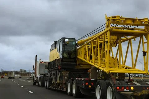 Heavy construction crane being transported on American highway in busy urban Stock Photos