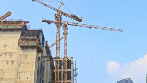 Heavy construction cranes working on concrete high-rise structure against blue Stock Footage 339758928