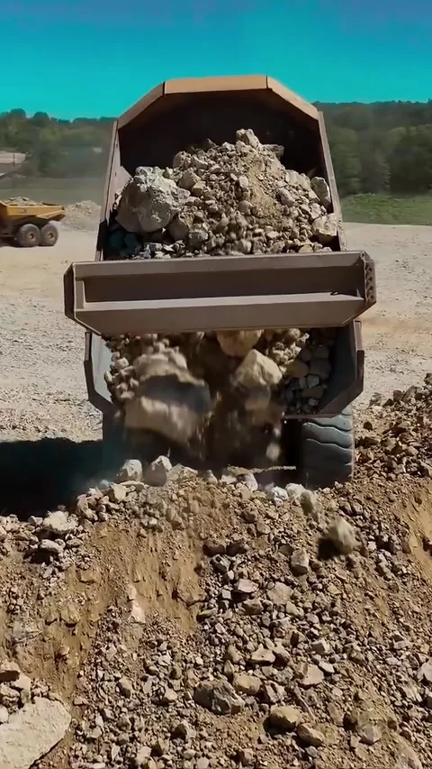 A Heavy Dump Truck Using Its Mechanism to Unload Large Rocks at a Busy Stock Footage 312223141
