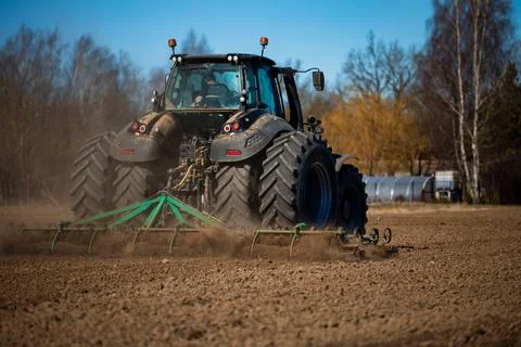 Heavy duty tractor pulls green harrow in dry field, spring tillage Stock Photos