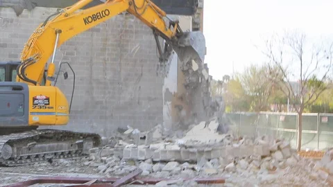 Heavy equipment tears down cinder block wall at demolition site Stock Footage 125056754
