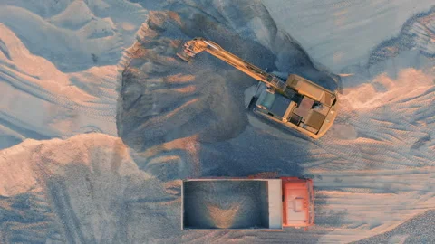 Heavy excavator loading crushed stone into orange dump truck in quarry Stock Footage 295697601