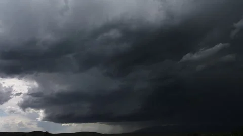 Heavy gray clouds darken to black at right of frame where a bolt of lightning Stock Footage 59525727
