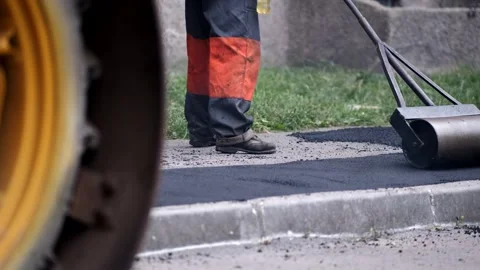 Heavy hand roller smoothing new asphalt pavement near yellow construction v.. Stock Footage 339801978