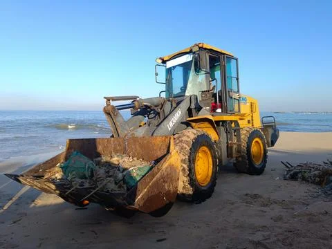 A heavy machine in operation to transport garbage on the beach. Stock Photos