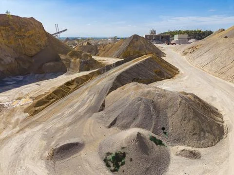 Heavy machinery is present at a construction site where large piles of sand a Stock Photos