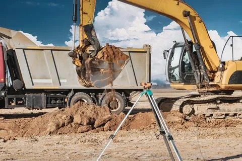 Heavy machinery is at work on a construction site. An excavator moves dirt wh Stock Photos