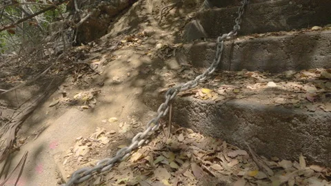 A heavy metal chain slides down a rugged outdoor staircase covered in dry leaves Stock Footage 294640454