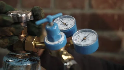 A heavy metallurgy worker opens opens gas cylinder valve with pressure gauge Stockbeeldmateriaal 143667280