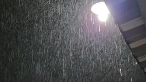 Heavy nighttime rain pouring down rapidly while illuminated by a glowing Stock Footage 334161832