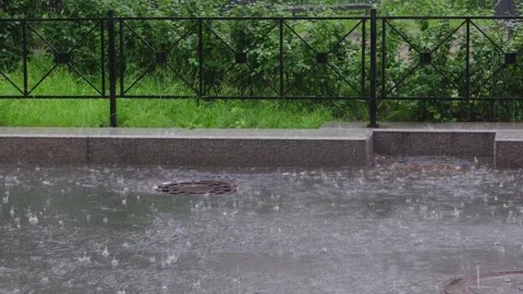 Heavy rain creates flowing water on urban street with drainage system Видео 339488828