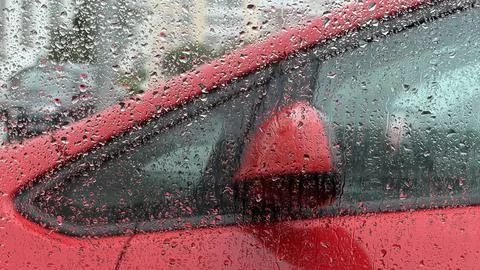 Heavy rain droplets clinging to a window pane, blurring the bright red color of Stock Photos