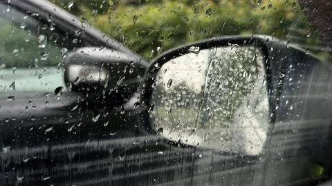 Heavy rain drops on a car window pane with a blurred view of a black side Stock Photos