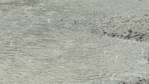 Heavy rain drops falling on a large puddle on concrete ground Stock Footage 338365218
